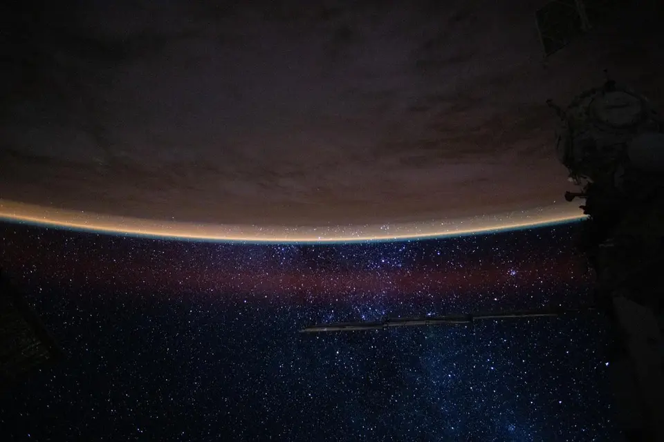 Céu estrelado sobre o horizonte da Terra, com o brilho alaranjado da atmosfera, visto da Estação Espacial