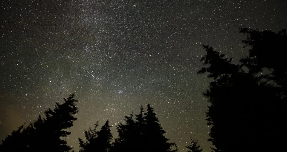 Meteoro riscando o céu noturno sobre uma paisagem escura durante uma chuva de meteoros