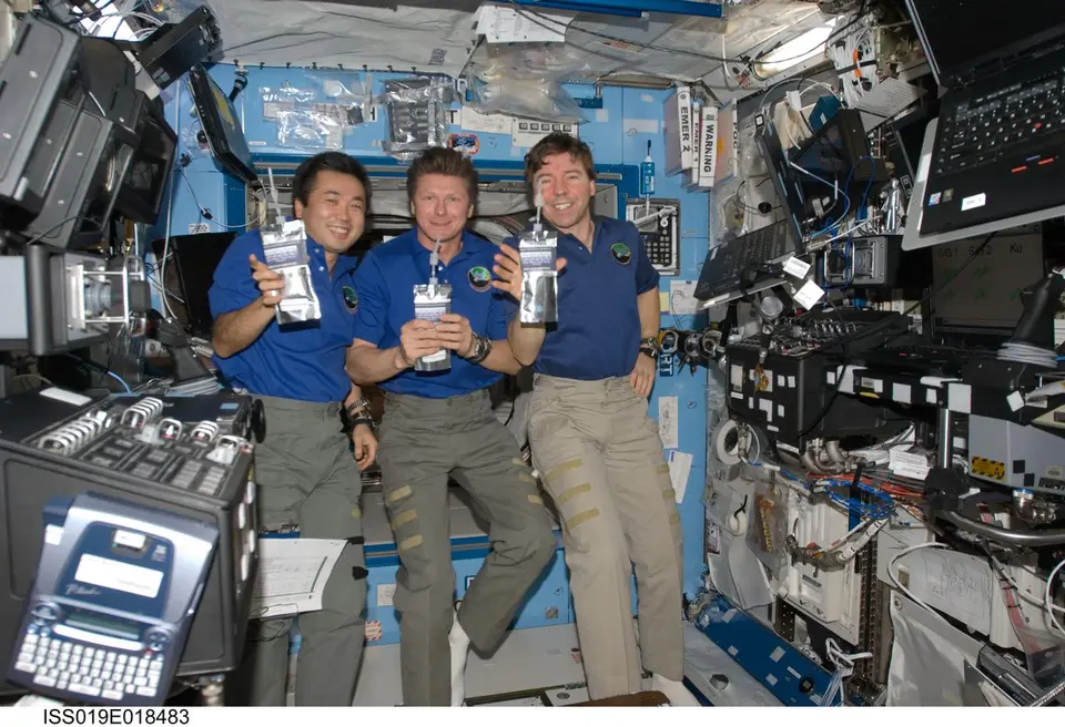 Astronauta bebendo água de um sachê com canudo dentro da Estação Espacial