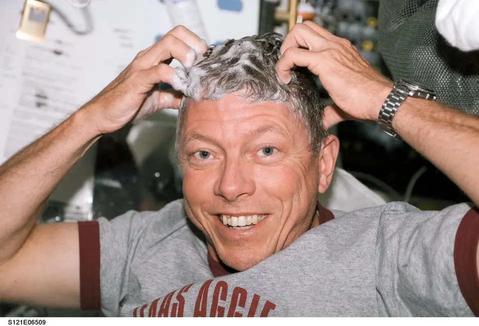Astronauta lavando o cabelo com xampu sem enxágue dentro da Estação Espacial
