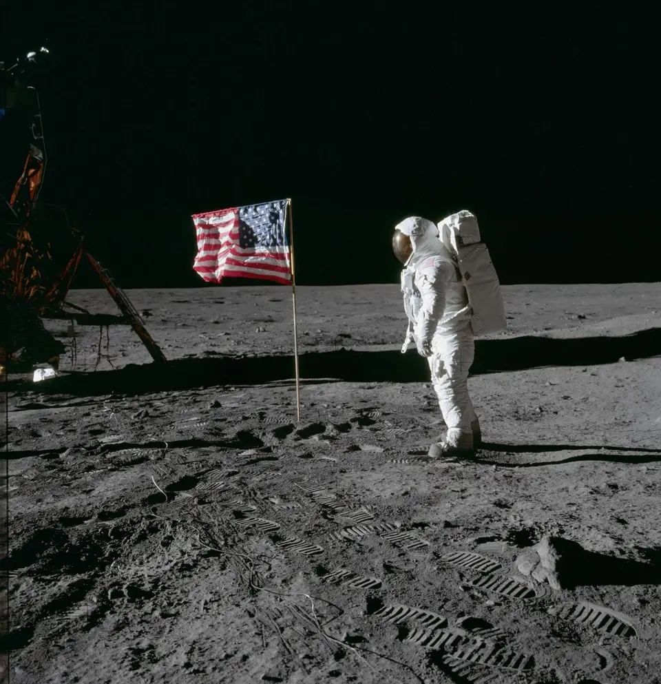 Astronauta da Apollo na superfície lunar ao lado da bandeira americana e do módulo lunar
