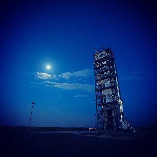 Torre de lançamento iluminada à noite, com a Lua no céu, antes de uma decolagem