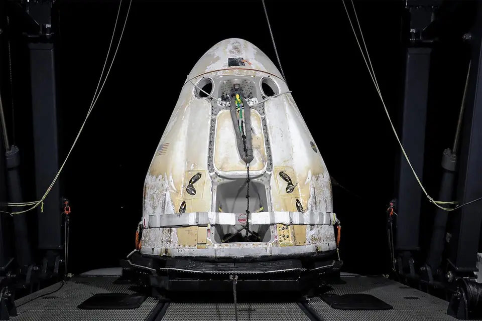 Cápsula Dragon da SpaceX descendo com paraquedas abertos sobre o oceano