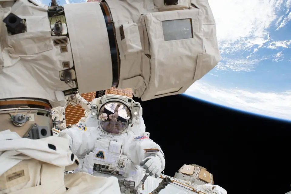 Astronauta em traje espacial branco durante caminhada espacial fora da Estação Espacial