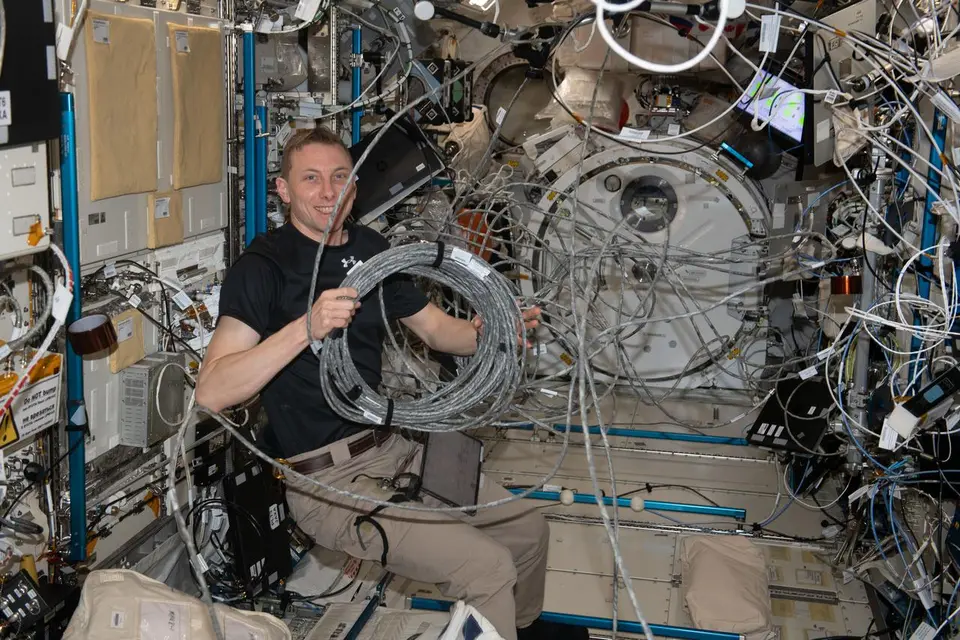Astronauta reconfigurando cabos e equipamentos dentro da Estação Espacial