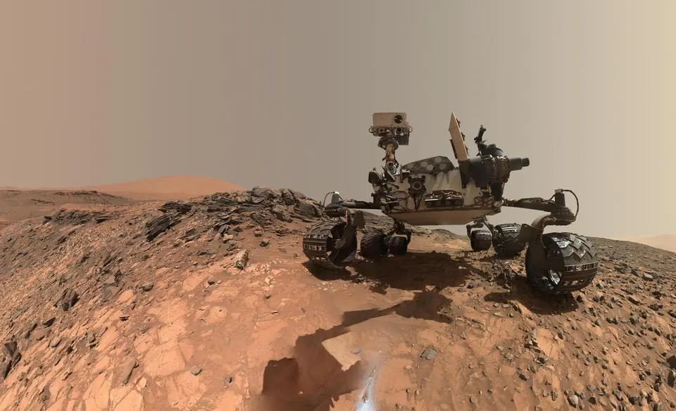 Autorretrato do rover Curiosity na superfície de Marte com montanhas ao fundo