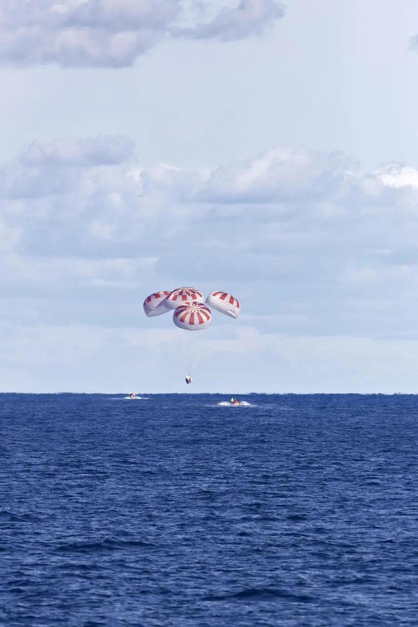 Cápsula Crew Dragon da SpaceX descendo com paraquedas abertos sobre o oceano